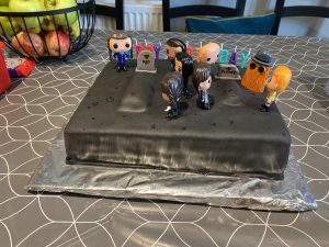Black fondant covered birthday cake with Addams Family figures, gravestone and graves